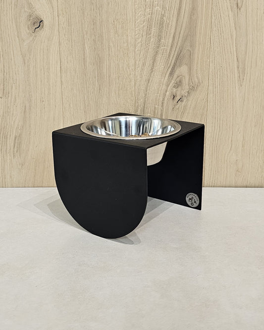 Black elevated pet feeder with a silver bowl on a light wood floor.
